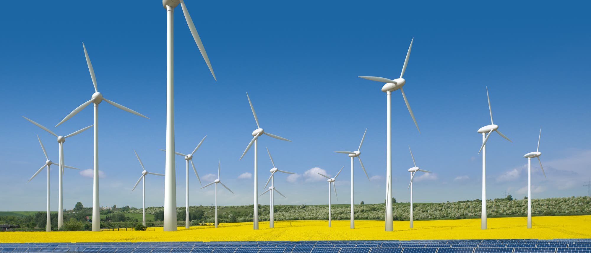 Windkrafträder und Solarmodule vor gleißend blauem Himmel, im Hintergrund gelbe Rapsfelder
