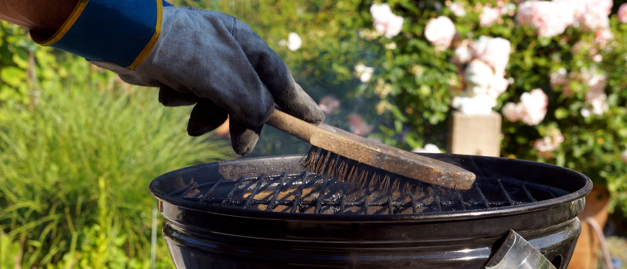 Eine Person mit Handschuhen reinigt einen Grillrost mit einer Drahtb&uuml;rste. 
