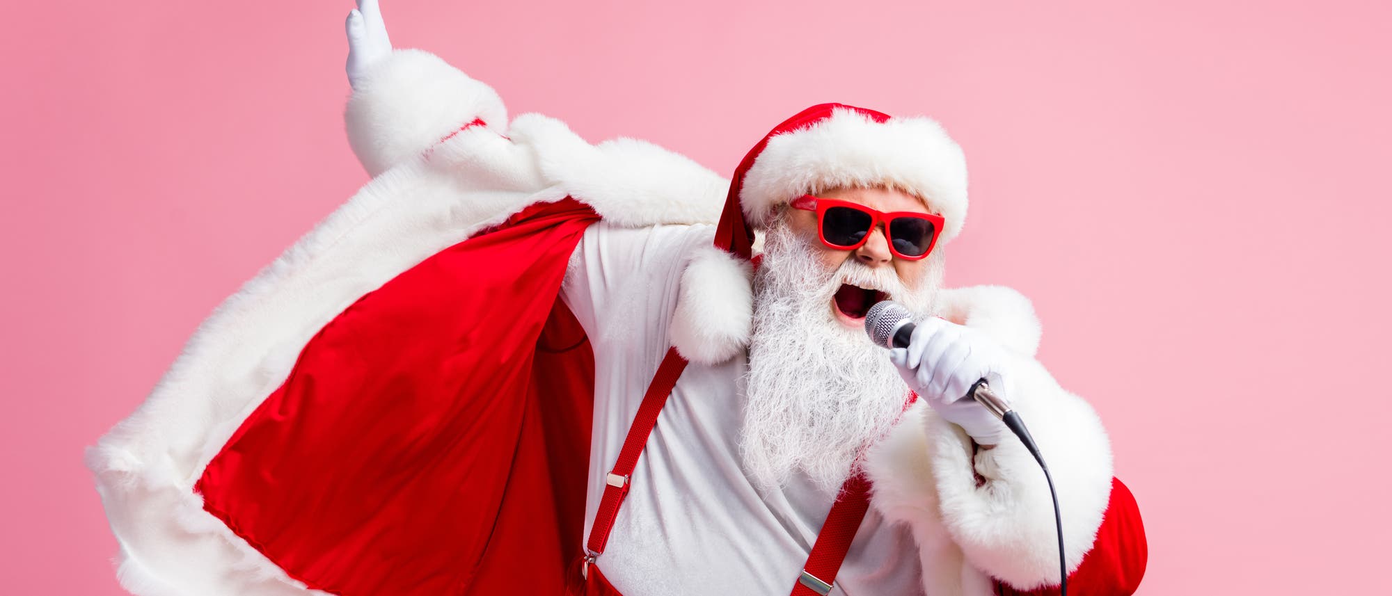 Ein Weihnachtsmann mit roter Sonnenbrille singt mit Mikrofon vor einem pinken Hintergrund 
