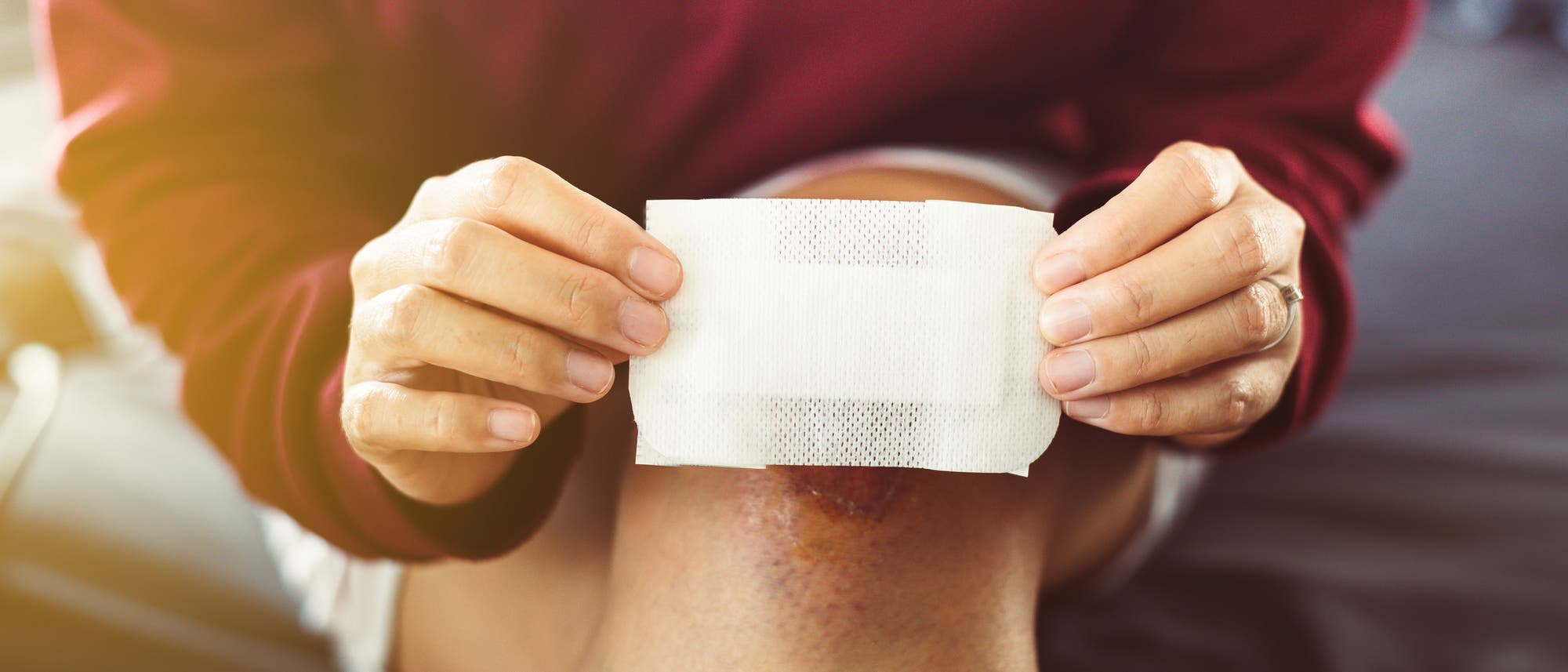 Eine Person h&auml;lt ein gro&szlig;es Pflaster &uuml;ber ein verletztes Knie. 