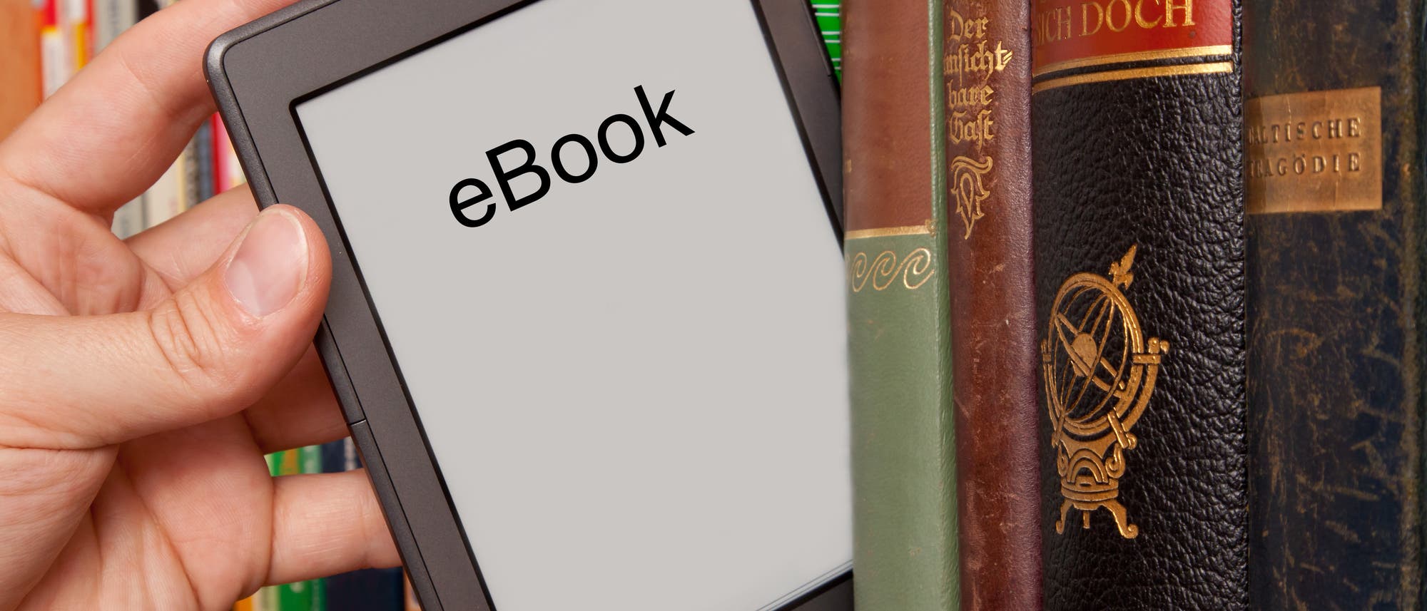 Eine Hand nimmt ein E-Book zwischen Büchern aus dem Bücherregal.