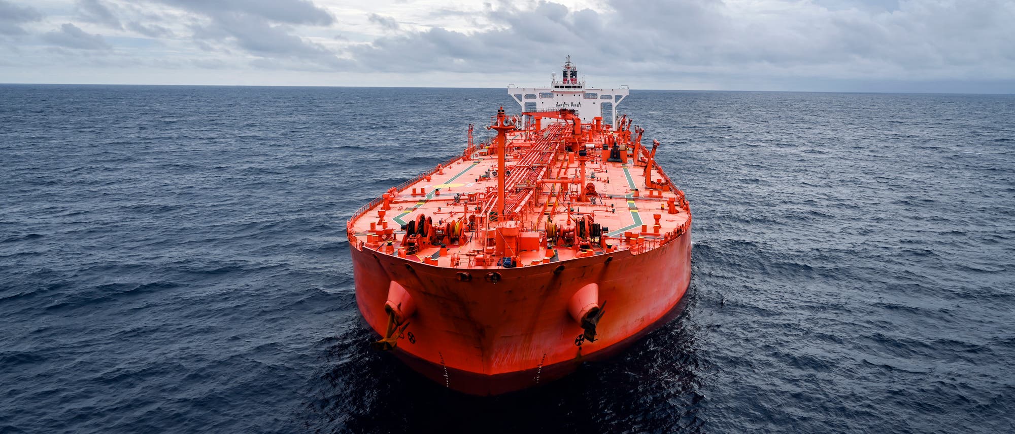 Ein gro&szlig;es, rotes Frachtschiff f&auml;hrt auf offenem Meer. Der Himmel ist bew&ouml;lkt, und das Wasser ist dunkelblau. Das Schiff ist zentral im Bild positioniert und zeigt seine Vorderseite. Auf dem Deck sind verschiedene Ausr&uuml;stungen und Strukturen sichtbar.