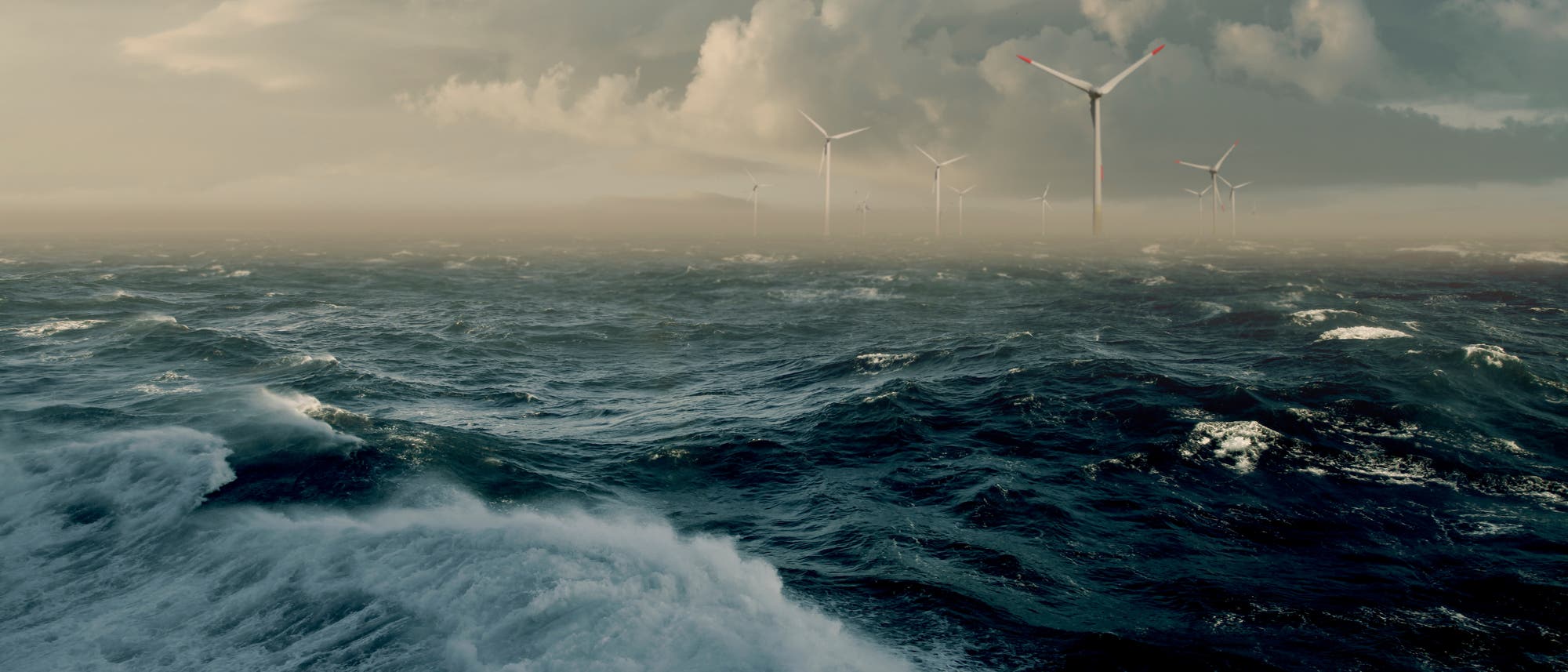 St&uuml;rmische Meereslandschaft mit mehreren Windkraftanlagen im Hintergrund. Die Windr&auml;der ragen aus dem Wasser und sind von dramatischen Wolken umgeben. Die Szene vermittelt eine Atmosph&auml;re von erneuerbarer Energiegewinnung in rauen Wetterbedingungen.