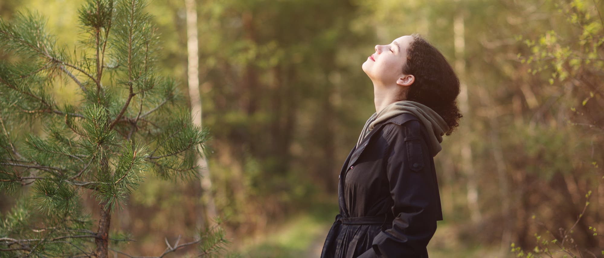 Eine Frau steht auf einer Waldlichtung, das Gesicht Richtung Himmel geneigt