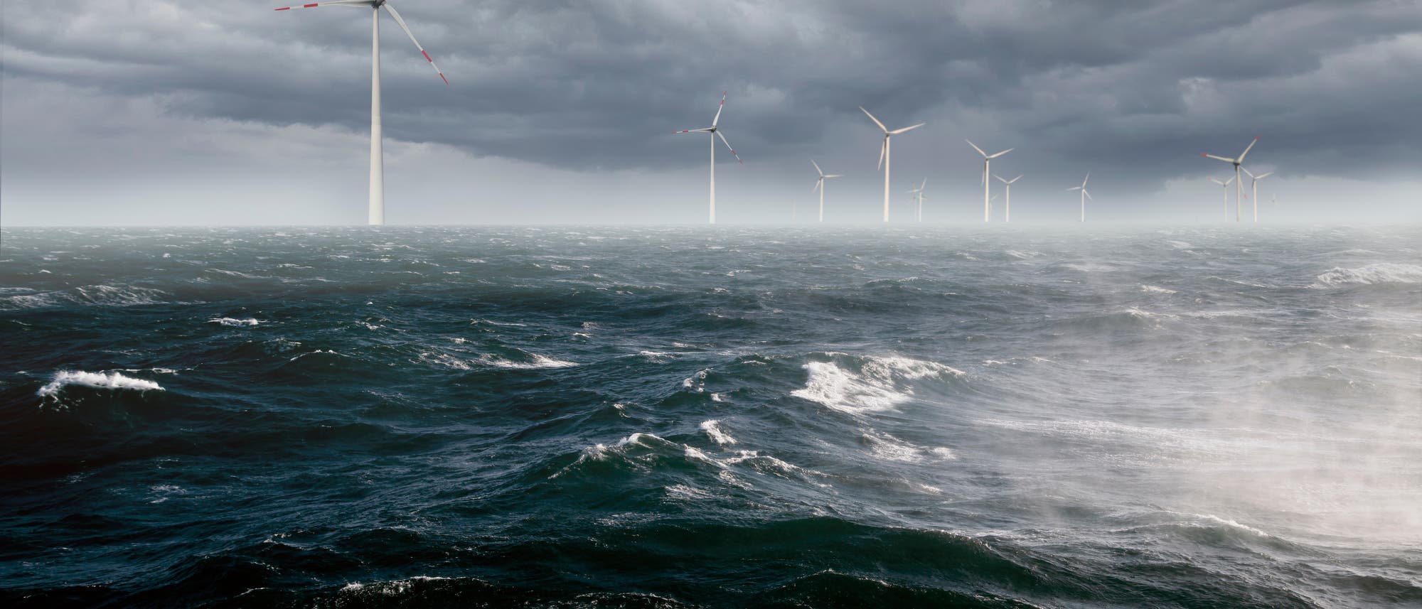 Offshore-Windpark bei stürmischem Wetter. Mehrere Windturbinen stehen im Meer unter einem dunkel und bedrohlich wirkenden bewölkten Himmel. Die Wellen sind hoch und der Wind stark. Offshore-Windpark bei stürmischem Wetter. Mehrere Windturbinen stehen im Meer unter einem dunkel und bedrohlich wirkenden bewölkten Himmel. Die Wellen sind hoch und der Wind stark.