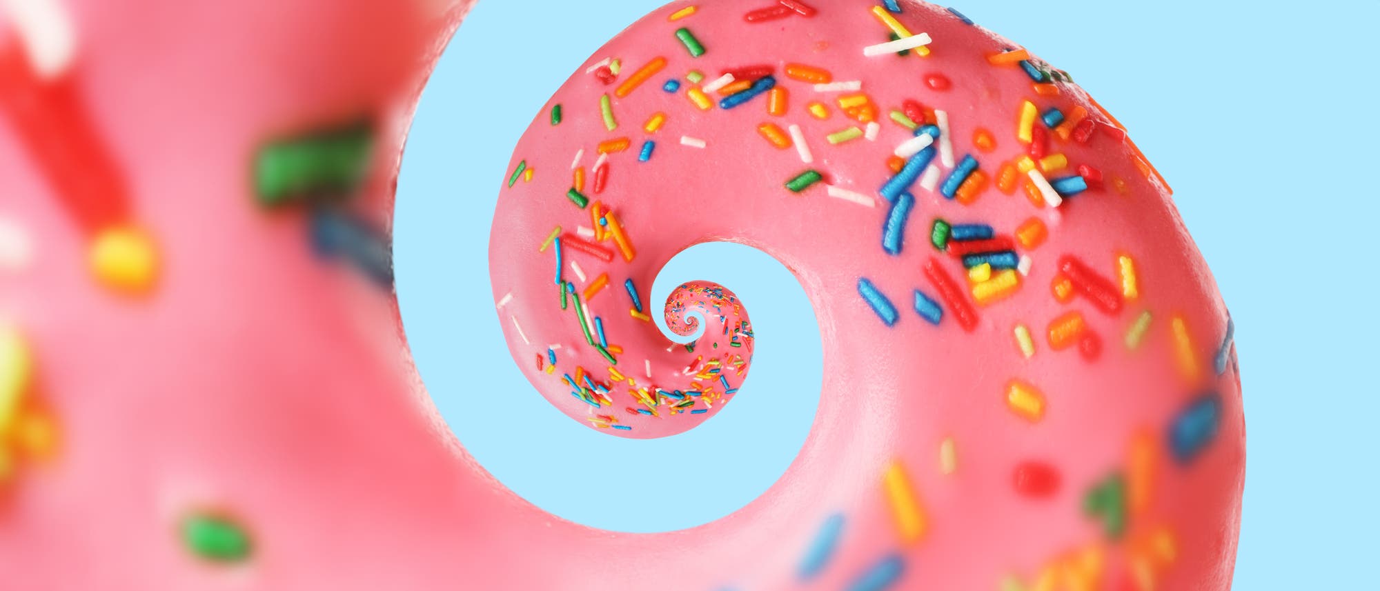 Ein spiralförmiges Bild eines rosafarbenen Donuts mit bunten Streuseln auf einem hellblauen Hintergrund. Die Spirale erzeugt einen hypnotischen Effekt, der den Blick in die Bildmitte zieht. Die leuchtenden Farben der Streusel kontrastieren mit dem rosa Zuckerguss und dem blauen Hintergrund. Ein spiralförmiges Bild eines rosafarbenen Donuts mit bunten Streuseln auf einem hellblauen Hintergrund. Die Spirale erzeugt einen hypnotischen Effekt, der den Blick in die Bildmitte zieht. Die leuchtenden Farben der Streusel kontrastieren mit dem rosa Zuckerguss und dem blauen Hintergrund.