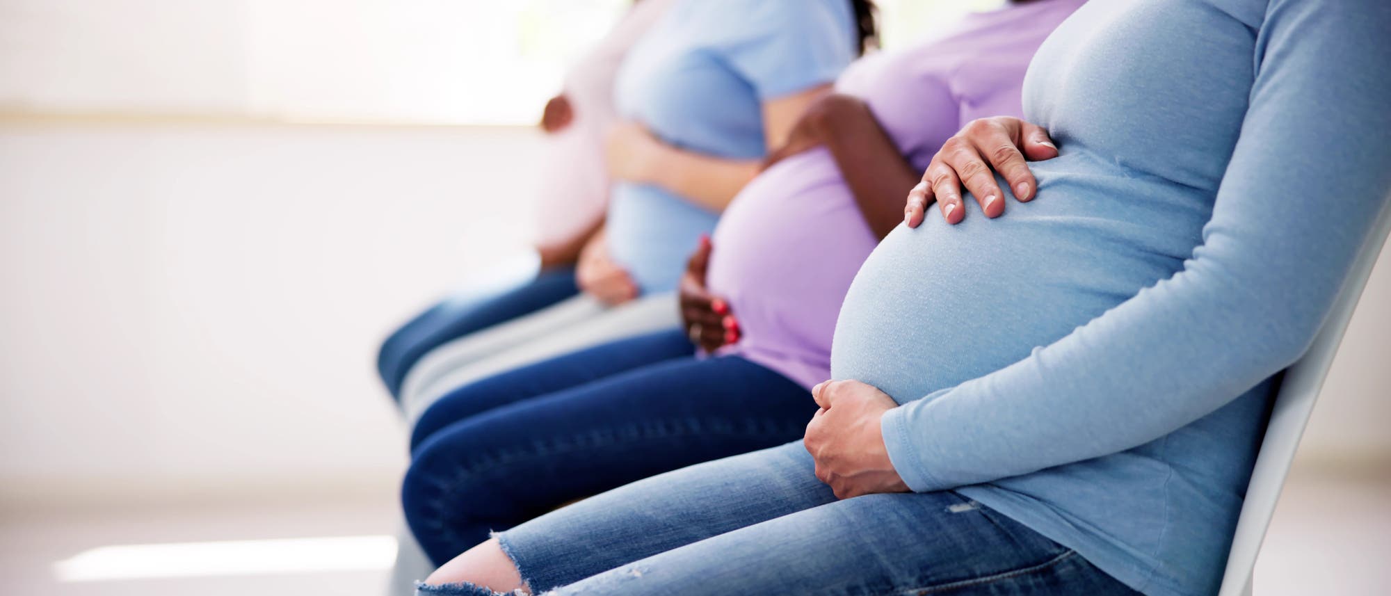 Vier schwangere Frauen sitzen in einer Reihe auf Stühlen in einem Wartezimmer