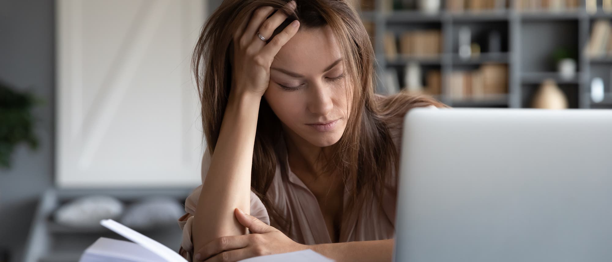 Eine junge Frau sitzt mit geschlossenen Augen und aufgestütztem Kopf vor dem Laptop.
