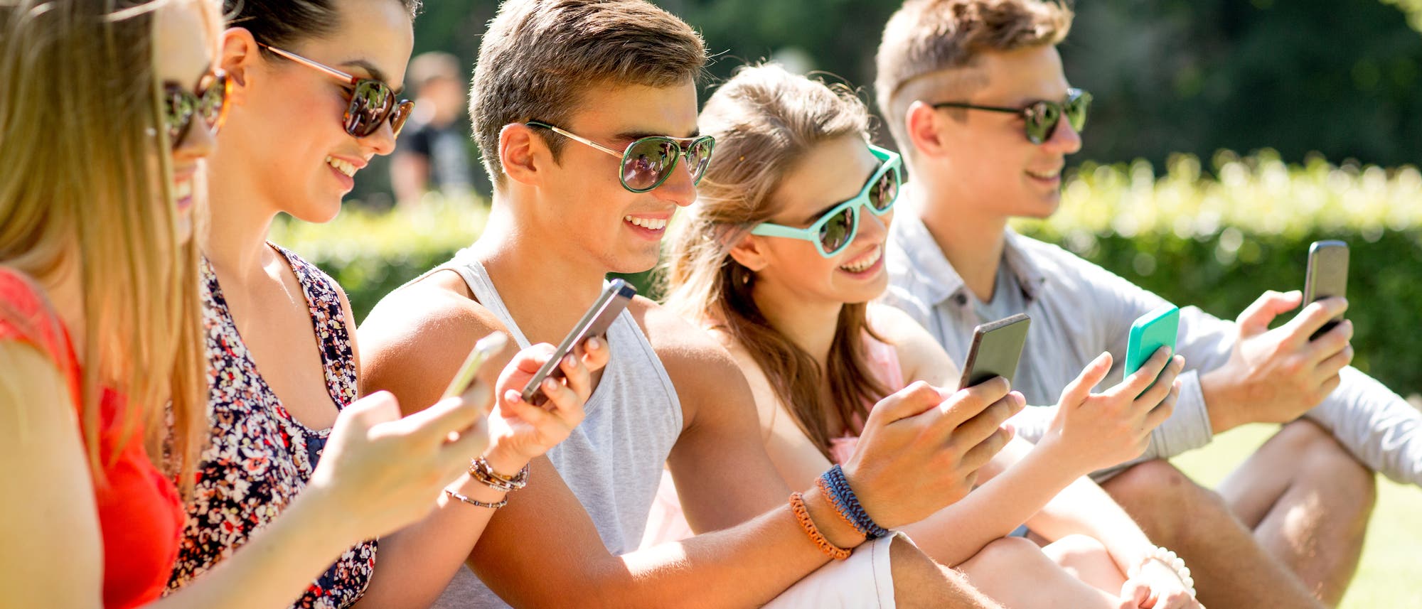 Junge Menschen sitzen mit Smartphone in der Sonne