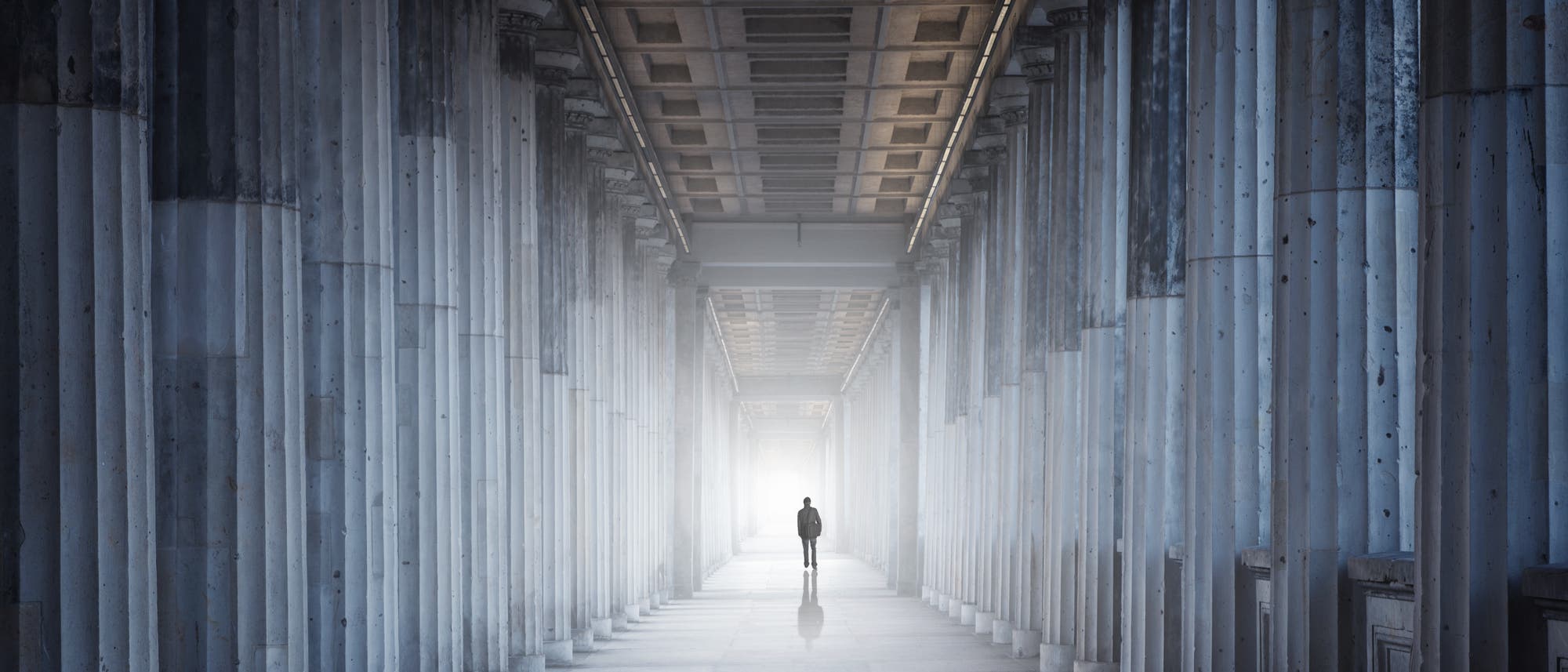 Eine sehr kleine menschliche Figur in einem sehr imposanten Säulengang. Symbolbild für Einsamkeit in der Wissenschaft oder gescheiterte Architektur.