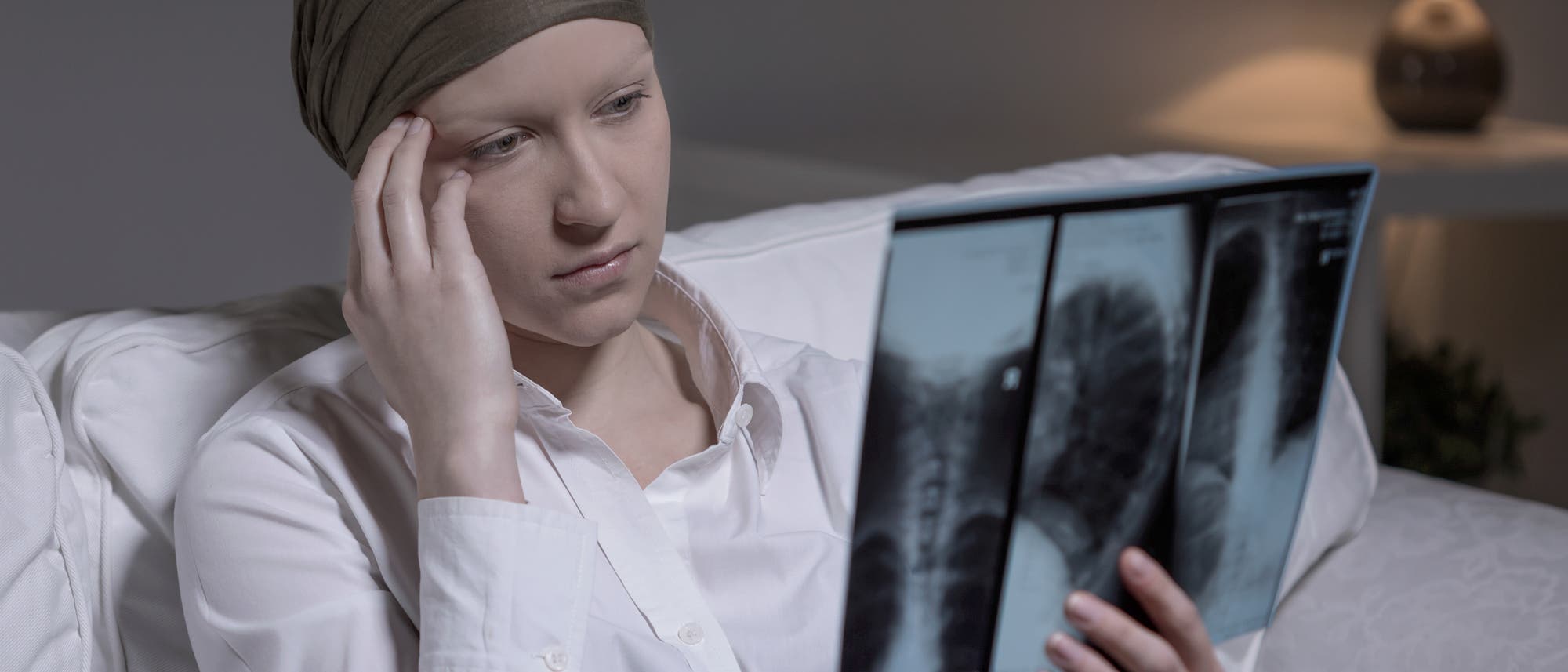 Eine junge Frau mit Kopftuch sitzt im Krankenhausbett und fasst sich an den Kopf, während sie ein Röntgenbild betrachtet. Krankenhäuser bieten erfahrungsgemäß eine große Auswahl von Anlässen, sich an den Kopf zu fassen.