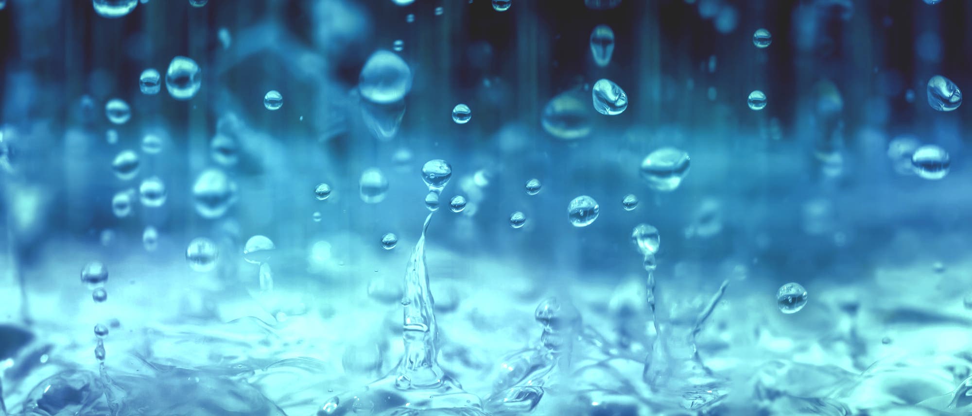 Nahaufnahme von fallenden Wassertropfen, die auf eine Wasseroberfl&auml;che treffen und Spritzer erzeugen. 