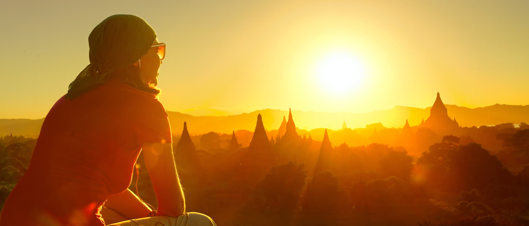Eine westliche Touristin blickt über die Tempel in den Sonnenuntergang von Bagan