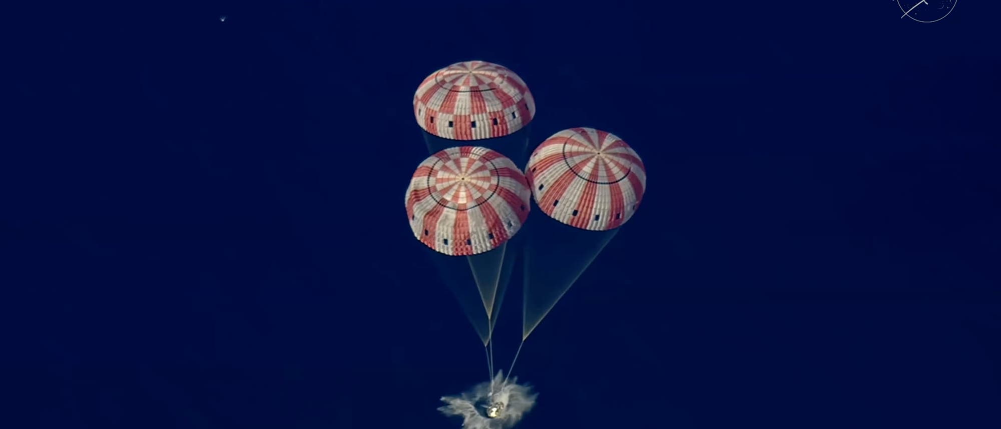 Drei gro&szlig;e, rot-wei&szlig; gestreifte Fallschirme bremsen die Raumkapsel Orion von Artemis 2 beim Abstieg &uuml;ber dem tiefblauen Hintergrund des Meeres. Oben rechts ist das NASA-Logo sichtbar. Die Fallschirme sind vollst&auml;ndig entfaltet und die Kapsel erzeugt eine leichte Gischt beim Kontakt mit der Wasseroberfl&auml;che.