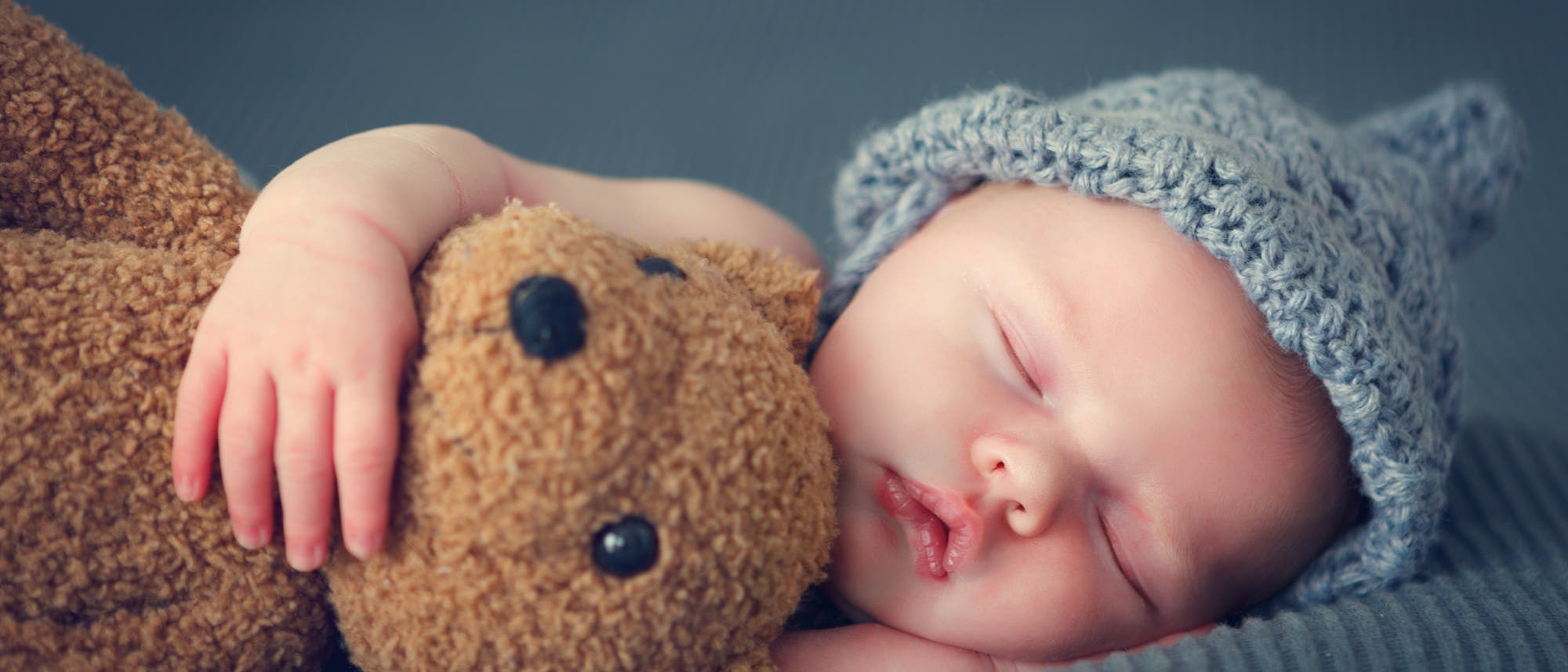 Schlafendes Baby mit Mütze und Stofftier 