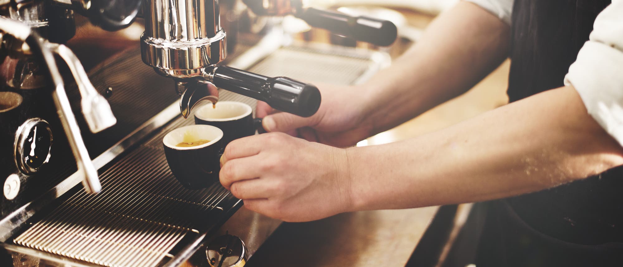 Zwei gefüllte Espressotassen unter der Düse einer Kaffeemaschine.