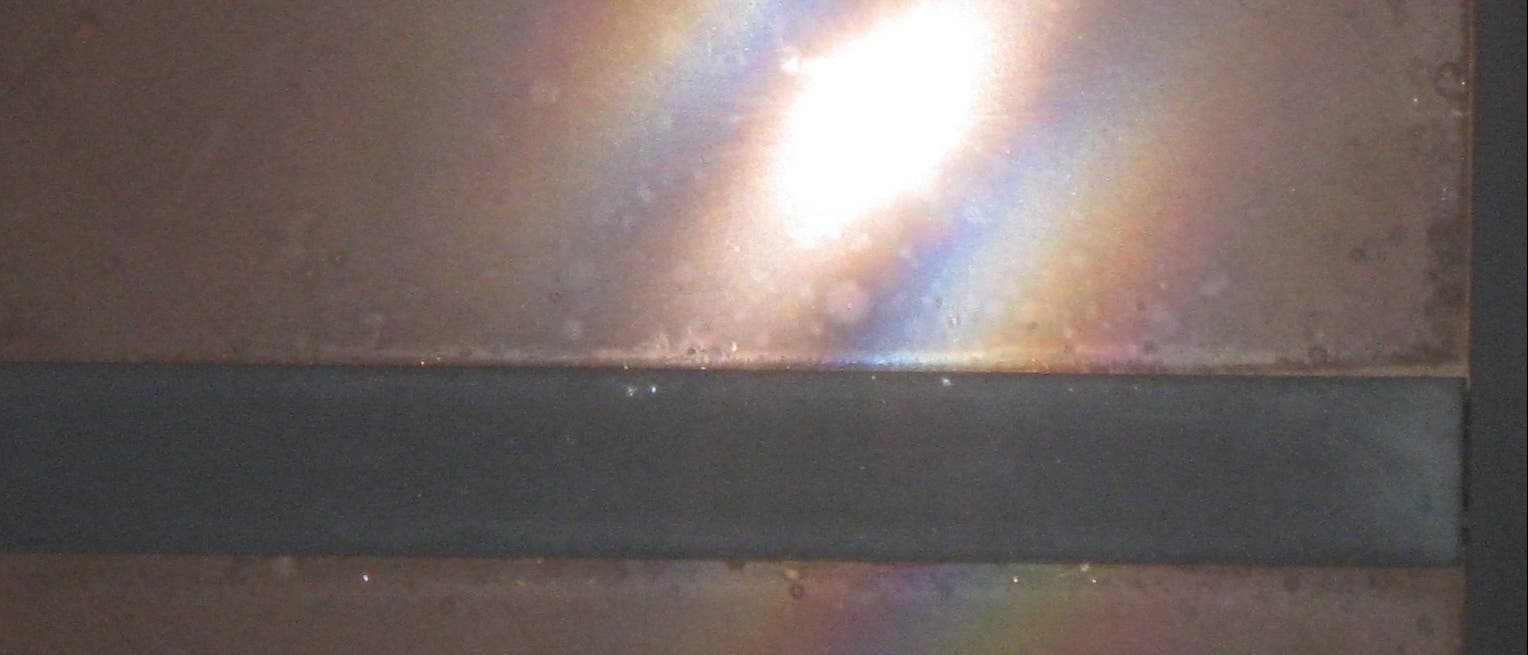 Ein verstaubtes Fenster zeigt Abschnitte bunter Ringe, die als leicht gekrümmte Streifen erscheinen