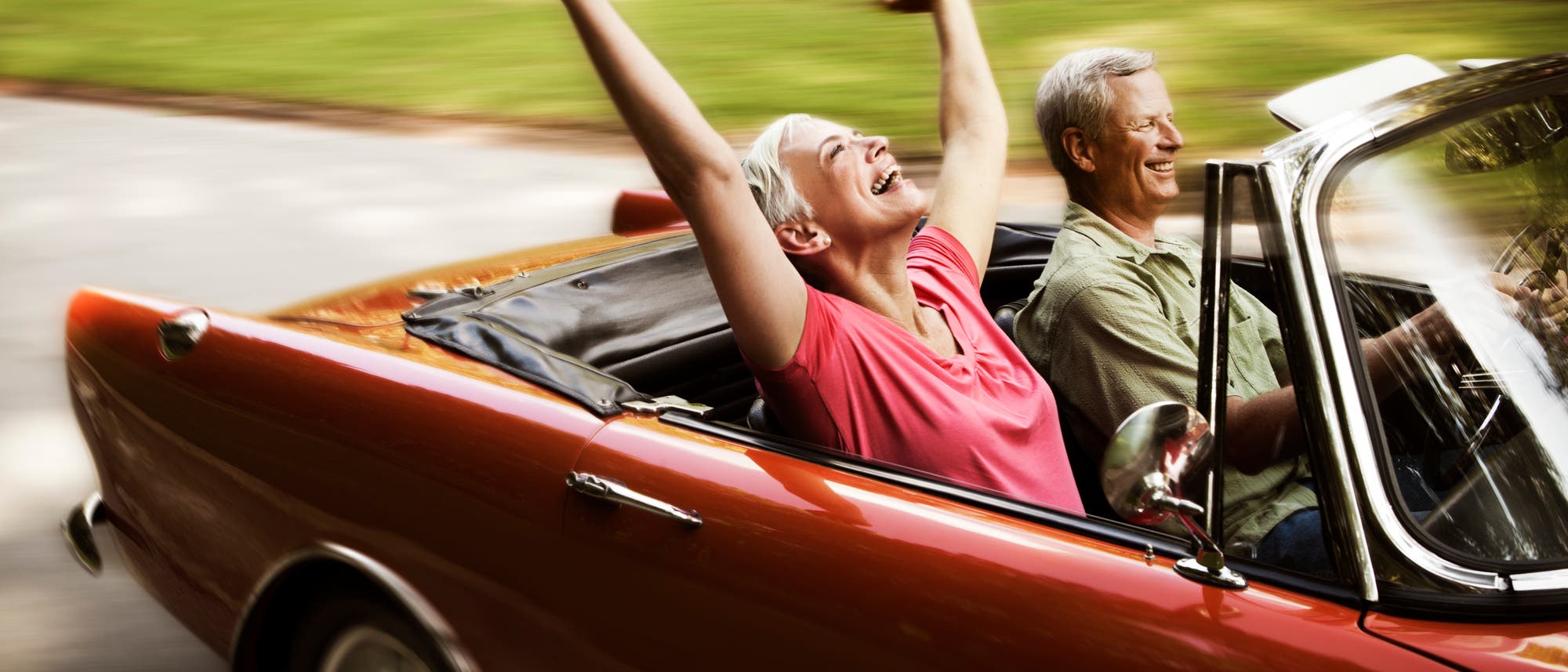 Ein glückliches älteres Paar fährt mit dem Cabrio in den Sonnenuntergang