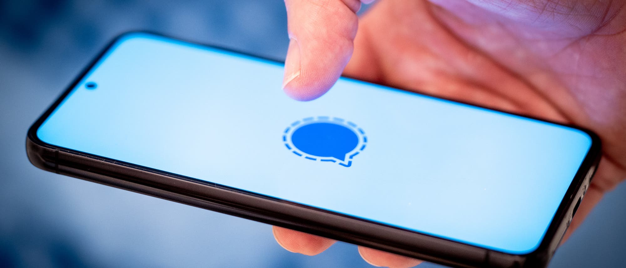 Eine Hand hält ein Smartphone, auf dessen Display das Logo des Signal-Messengers auf weißem Hintergrund erscheint