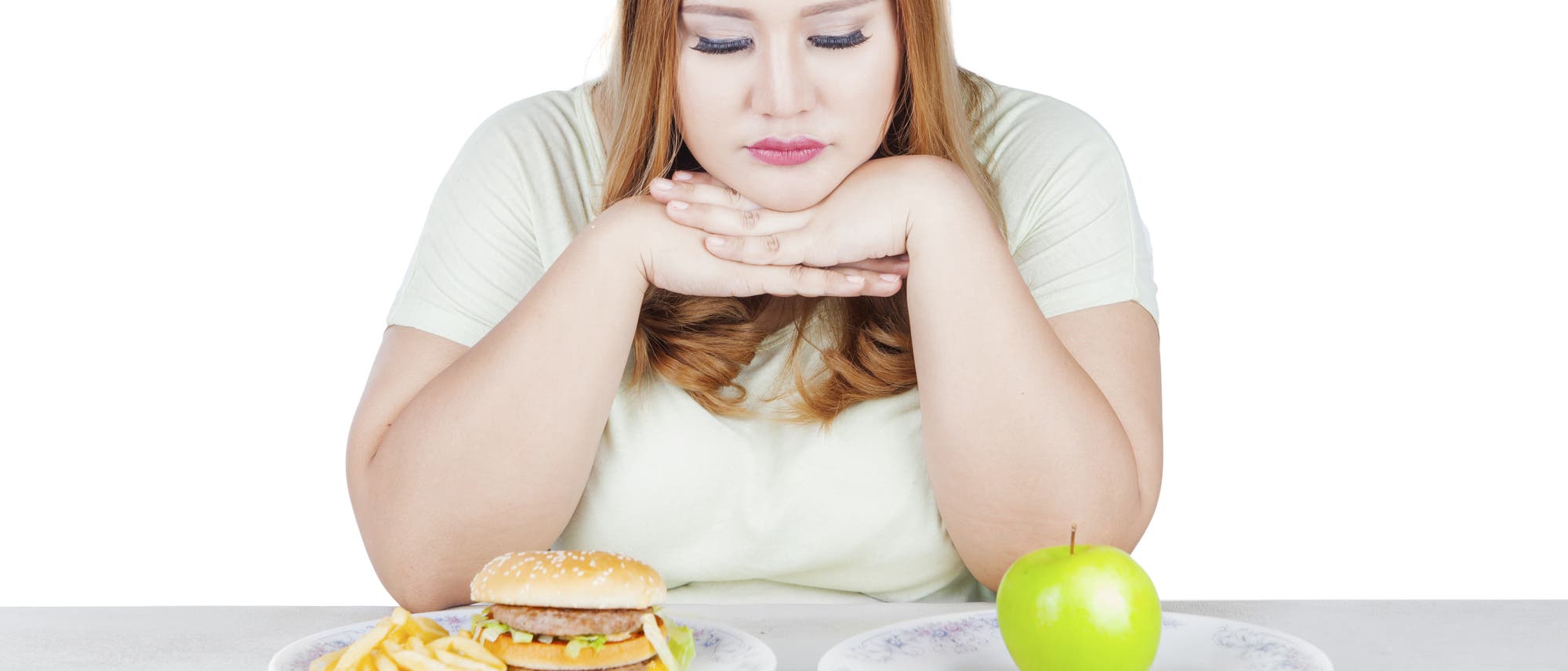 Eine Frau sitzt vor einem Burger und einem Apfel, sie muss sich scheinbar entscheiden