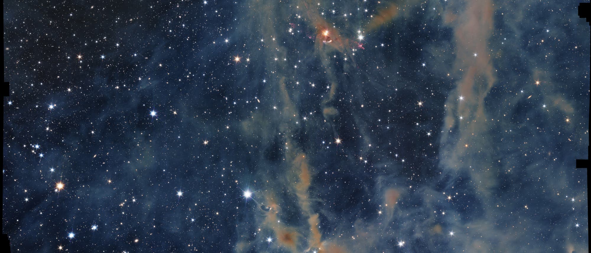 Ein Bild des Weltraums, das einen dichten Sternenhimmel mit zahlreichen leuchtenden Sternen zeigt. Im Vordergrund sind farbige Gas- und Staubwolken zu sehen, die in Blau- und Orangetönen leuchten. Diese Wolken bilden komplexe Strukturen und verleihen dem Bild eine dynamische Tiefe. Der Hintergrund ist dunkel, was die Helligkeit der Sterne und die Details der Nebel betont. Das Bild vermittelt die Weite und Schönheit des Universums.