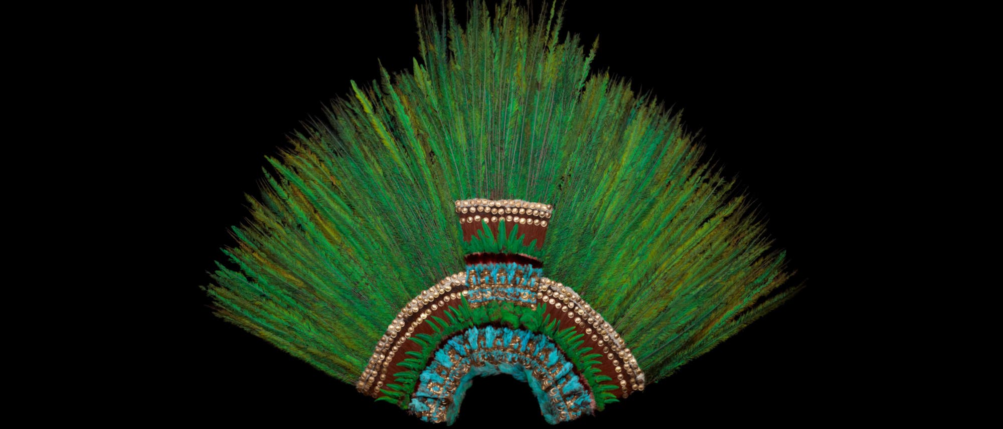 Ein traditioneller Kopfschmuck aus grünen Federn, die fächerförmig angeordnet sind. Der Kopfschmuck ist mit goldenen und roten Details verziert und hat eine symmetrische Struktur. Der Hintergrund ist schwarz, was die Farben des Kopfschmucks hervorhebt.