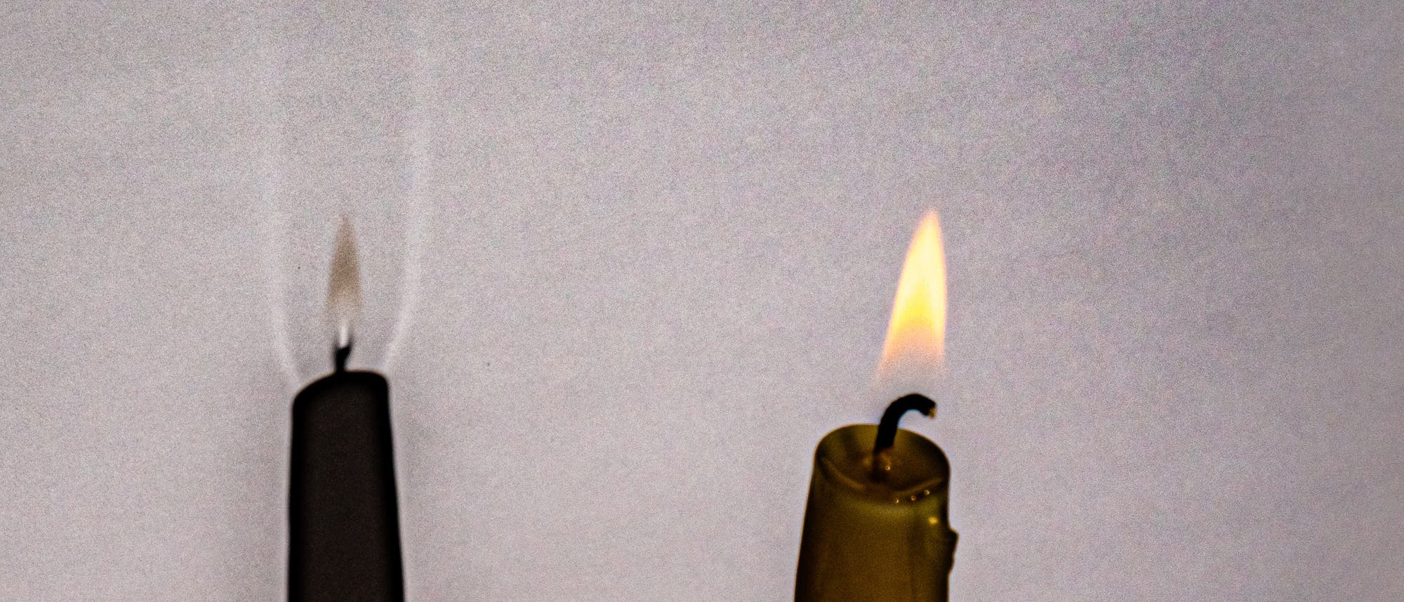 Eine brennende Kerze wirft einen Schatten auf eine weiße Fläche. Der Schatten der Leuchtzone ist leicht bräunlich, während im Kern auf Höhe des Dochts sowie seitlich der Abgasfahne helle Bereiche zu erkennen sind.