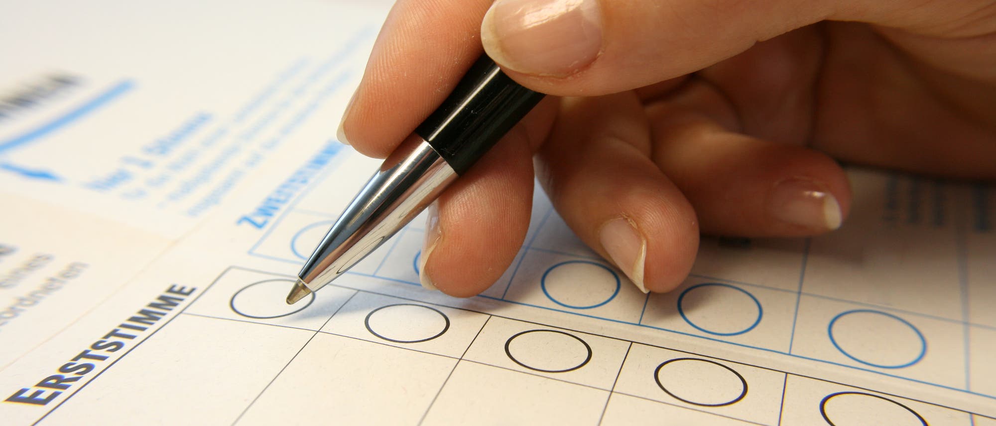 Eine Hand mit Stift kreuzt auf einem Wahlzettel für die Bundestagswahl ein Feld an.