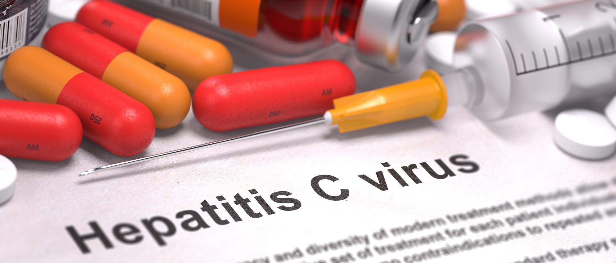 Symbolbild mit Tabletten und Spritzen und einem Zettel, auf dem "Hepatitis C Virus" steht.