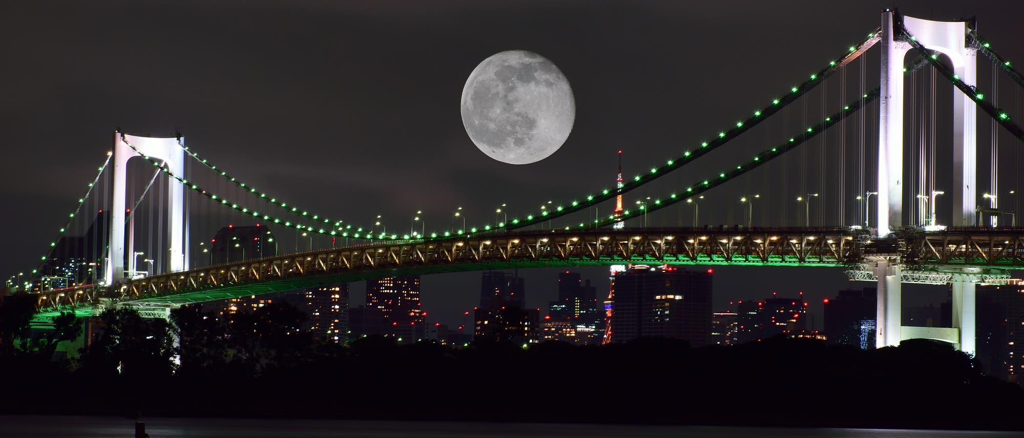 Mond über einer bunt beleuchteten Hängebrücke im Hafen von Tokio
