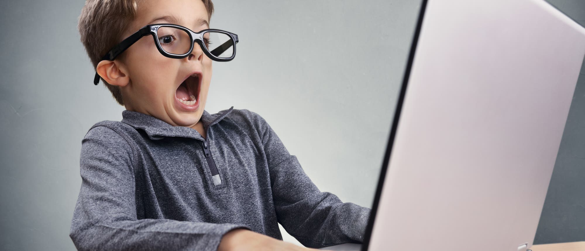 Kind mit Hemd und Brille sitzt vor einem Monitor und guckt übertrieben erschrocken