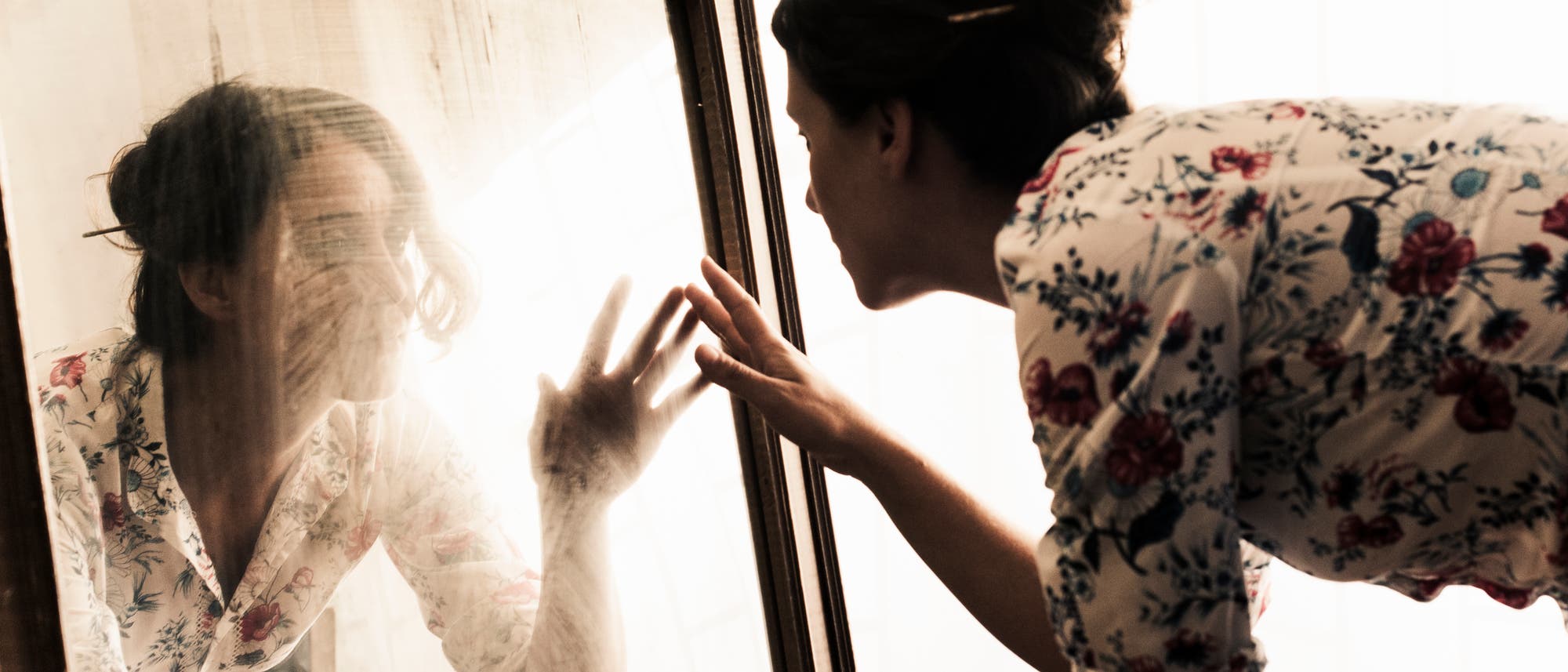 Eine Frau kniet vor einem Spiegel und streckt die Hand nach ihrem Spiegelbild aus.