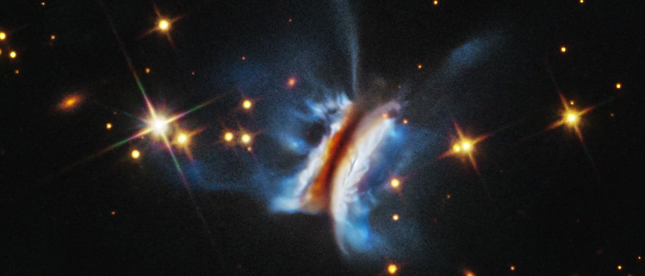 Ein leuchtender planetarischer Nebel im Weltraum, umgeben von zahlreichen funkelnden Sternen. Der Nebel zeigt eine symmetrische, fl&uuml;gelartige Struktur mit blauen und orangefarbenen T&ouml;nen, die von einem zentralen, hellen Bereich ausgehen. Die Sterne im Hintergrund sind gleichm&auml;&szlig;ig verteilt und variieren in Helligkeit. Der dunkle Hintergrund hebt die Farben und Formen des Nebels hervor.