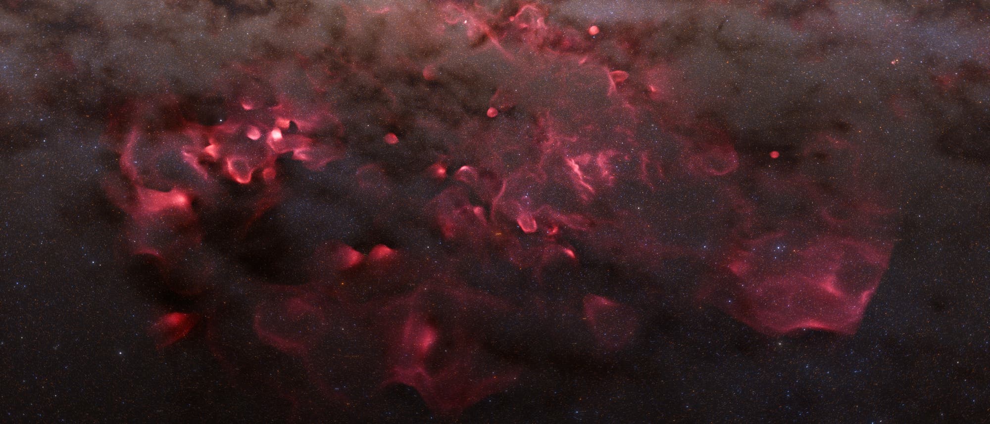 Una grabación astronómica muestra una vasta nube de gas rojizo y brillante en el espacio, rodeada de nubes de polvo oscuro y un fondo de numerosas estrellas pequeñas. Las áreas rojas indican gases de hidrógeno ionizados, que son estimulados para brillar por estrellas cercanas. La estructura de la nube es irregular y tiene diferentes áreas de densidad que son visibles a través de contrastes oscuros y brillantes. Una grabación astronómica muestra una vasta nube de gas rojizo y brillante en el espacio, rodeada de nubes de polvo oscuro y un fondo de numerosas estrellas pequeñas. Las áreas rojas indican gases de hidrógeno ionizados, que son estimulados para brillar por estrellas cercanas. La estructura de la nube es irregular y tiene diferentes áreas de densidad que son visibles a través de contrastes oscuros y brillantes.