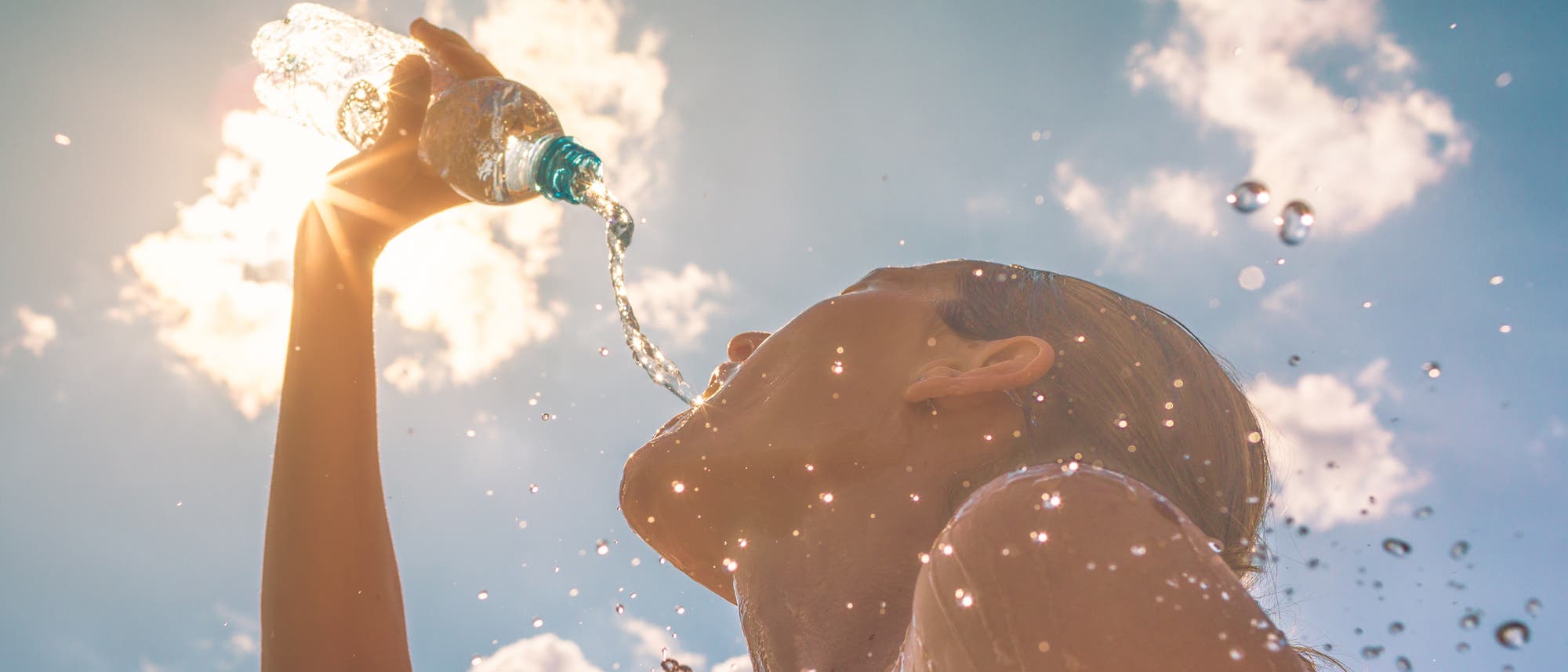 Eine Person trinkt an einem sonnigen Tag Wasser aus einer Plastikflasche. Der Himmel ist blau mit einigen Wolken, und Sonnenstrahlen scheinen durch die Flasche. Wassertropfen spritzen in die Luft. Die Szene vermittelt ein Gefühl von Erfrischung und Sommer. Eine Person trinkt an einem sonnigen Tag Wasser aus einer Plastikflasche. Der Himmel ist blau mit einigen Wolken, und Sonnenstrahlen scheinen durch die Flasche. Wassertropfen spritzen in die Luft. Die Szene vermittelt ein Gefühl von Erfrischung und Sommer.