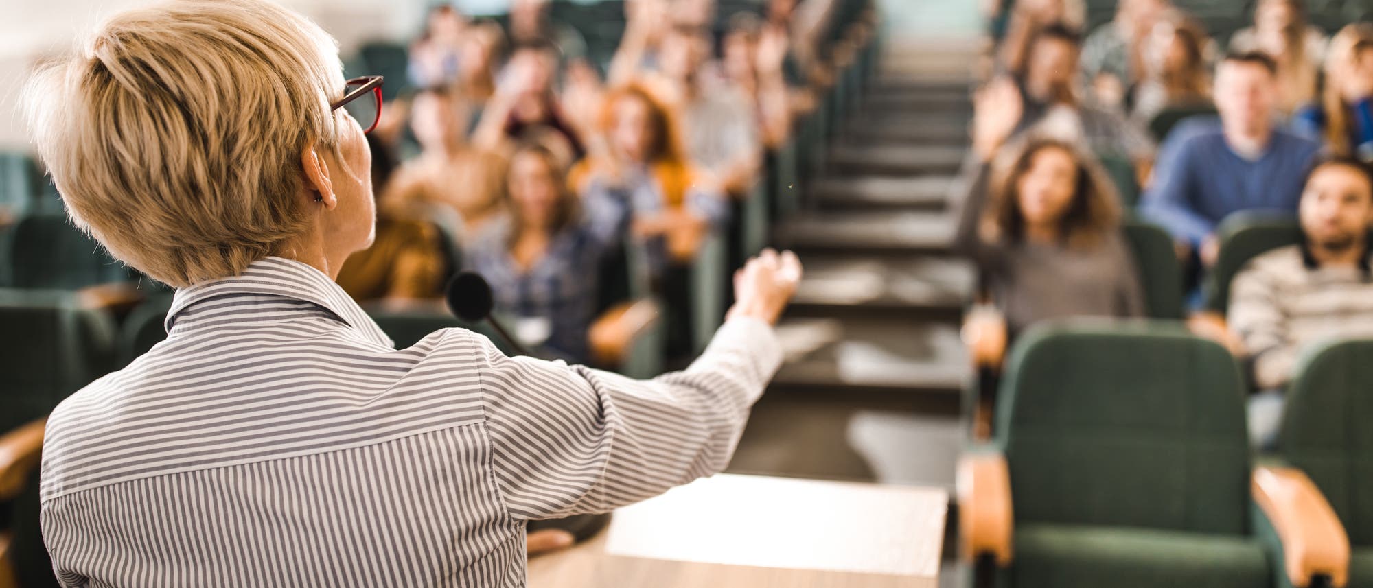 Eine Person steht an einem Rednerpult in einem Hörsaal und spricht zu einem Publikum. Die Zuhörer sitzen in Reihen und einige heben die Hand, möglicherweise um Fragen zu stellen. Die Atmosphäre wirkt konzentriert und lehrreich. Eine Person steht an einem Rednerpult in einem Hörsaal und spricht zu einem Publikum. Die Zuhörer sitzen in Reihen und einige heben die Hand, möglicherweise um Fragen zu stellen. Die Atmosphäre wirkt konzentriert und lehrreich.