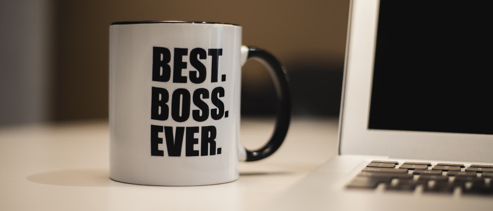 Eine Tasse mit der Aufschrift »Best. Boss. Ever.« steht auf einem Tisch neben einem Laptop