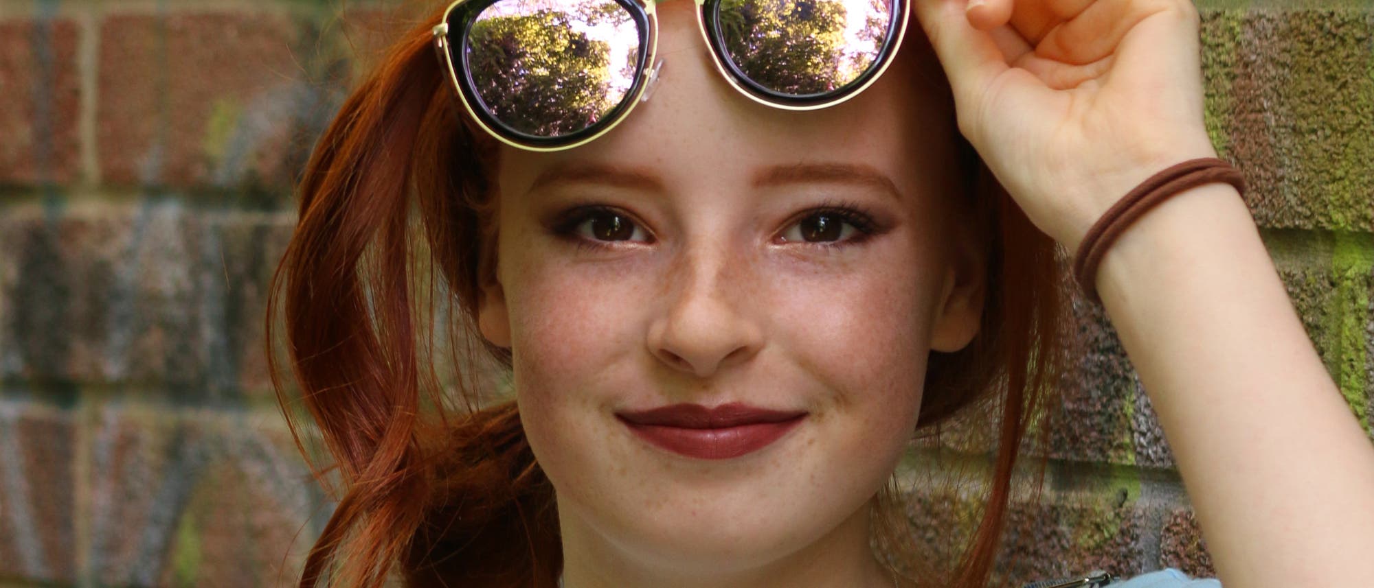 Junge Frau mit roten Haaren, dunklen Augen und Sommersprossen und einer Sonnenbrille über der Stirn