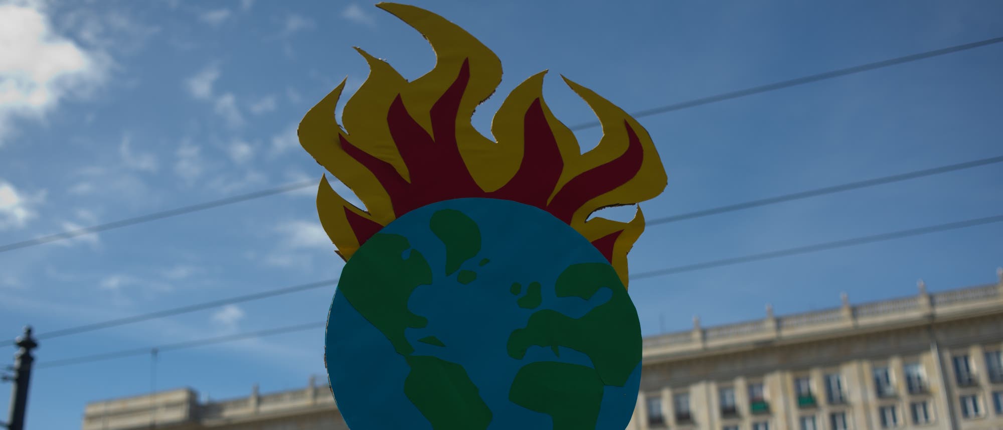 Eine stilisierte Darstellung der Erde mit Flammen, die aus der oberen Hälfte lodern, symbolisiert die globale Erwärmung. Der Hintergrund zeigt einen blauen Himmel mit einigen Wolken und ein Gebäude am unteren Rand. Eine stilisierte Darstellung der Erde mit Flammen, die aus der oberen Hälfte lodern, symbolisiert die globale Erwärmung. Der Hintergrund zeigt einen blauen Himmel mit einigen Wolken und ein Gebäude am unteren Rand.