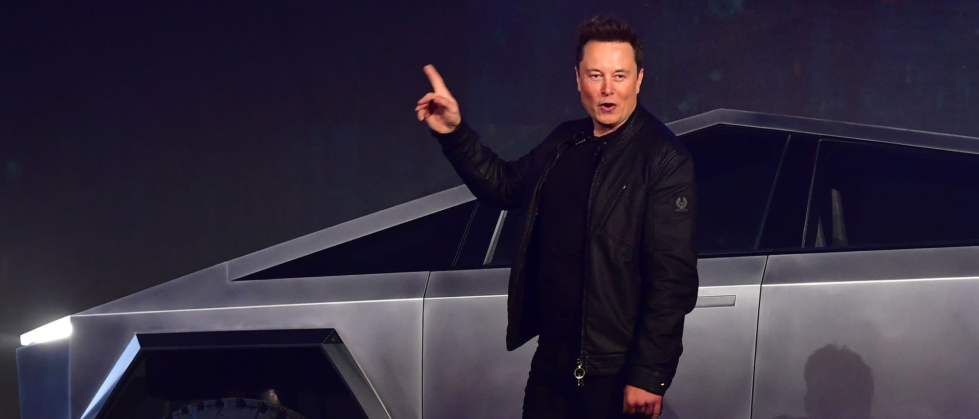 Tesla-CEO Elon Musk steht vor einem futuristisch aussehenden Fahrzeug mit kantigem Design und großen Reifen, einem Tesla Cybertruck. Er hebt einen Finger, als ob er etwas erklärt oder präsentiert. Das Fahrzeug hat eine silberne, metallische Oberfläche und leuchtende Scheinwerfer. Tesla-CEO Elon Musk steht vor einem futuristisch aussehenden Fahrzeug mit kantigem Design und großen Reifen, einem Tesla Cybertruck. Er hebt einen Finger, als ob er etwas erklärt oder präsentiert. Das Fahrzeug hat eine silberne, metallische Oberfläche und leuchtende Scheinwerfer.
