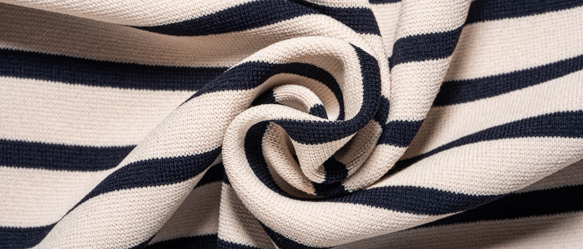 Ein Stoff mit dunkelblauen und cremefarbenen Streifen ist in der Mitte zu einer Spirale gedreht. Die Textur des Materials ist deutlich sichtbar. Ein Stoff mit dunkelblauen und cremefarbenen Streifen ist in der Mitte zu einer Spirale gedreht. Die Textur des Materials ist deutlich sichtbar.