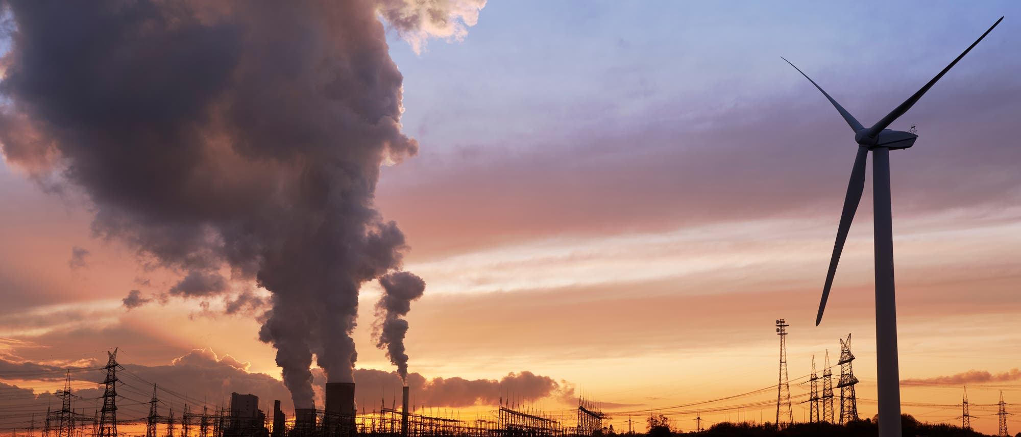 Windenergieanlage und Rauch aus Kohlekraftwerke vor Abendhimmel 