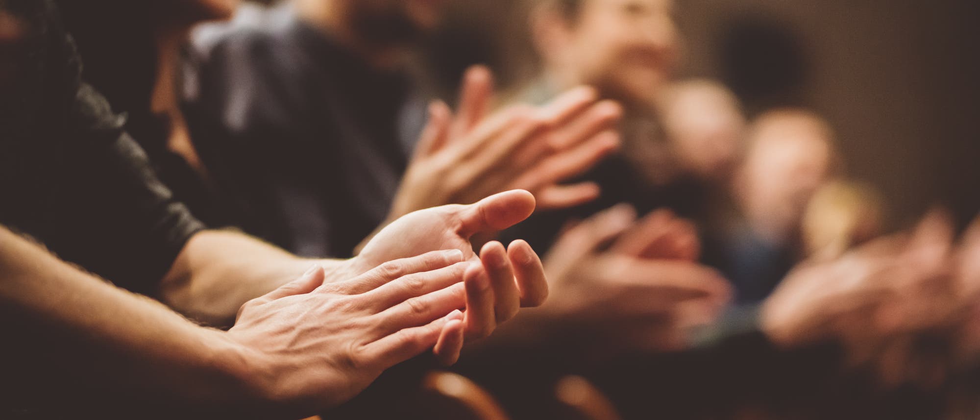 Eine Gruppe von Menschen sitzt in einem Auditorium und applaudiert. Die Hände im Vordergrund sind scharf gestellt, während die Gesichter im Hintergrund unscharf sind. Eine Gruppe von Menschen sitzt in einem Auditorium und applaudiert. Die Hände im Vordergrund sind scharf gestellt, während die Gesichter im Hintergrund unscharf sind.