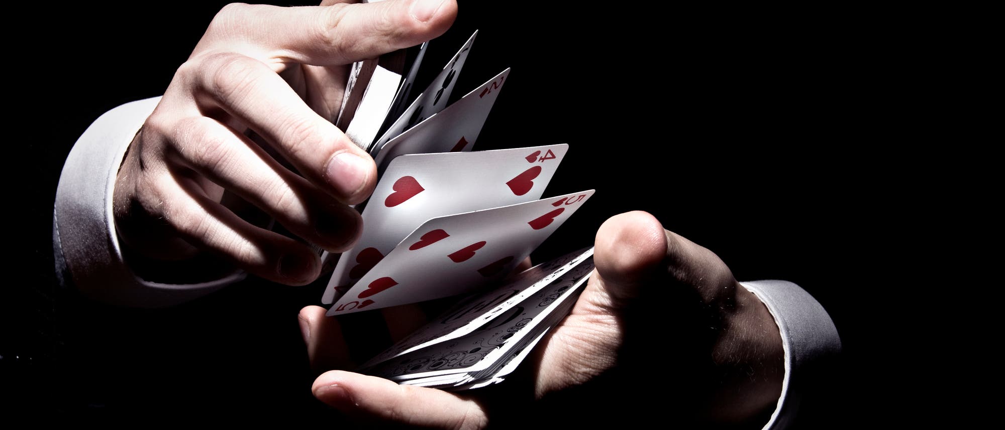 Eine Person in einem Anzug führt einen Kartentrick vor, bei dem Spielkarten mit Herzsymbolen in der Luft schweben. Die Szene ist in einem dunklen Hintergrund gehalten, wodurch die Karten und Hände im Vordergrund hervorgehoben werden. Die Karten sind teilweise sichtbar und scheinen in Bewegung zu sein, was auf Geschicklichkeit und Präzision hinweist. Eine Person in einem Anzug führt einen Kartentrick vor, bei dem Spielkarten mit Herzsymbolen in der Luft schweben. Die Szene ist in einem dunklen Hintergrund gehalten, wodurch die Karten und Hände im Vordergrund hervorgehoben werden. Die Karten sind teilweise sichtbar und scheinen in Bewegung zu sein, was auf Geschicklichkeit und Präzision hinweist.
