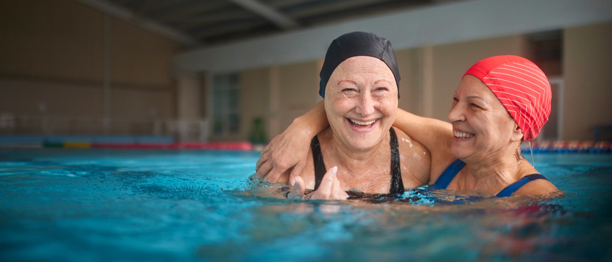 Zwei Seniorinnen umarmen sich im Wasser im Hallenbad