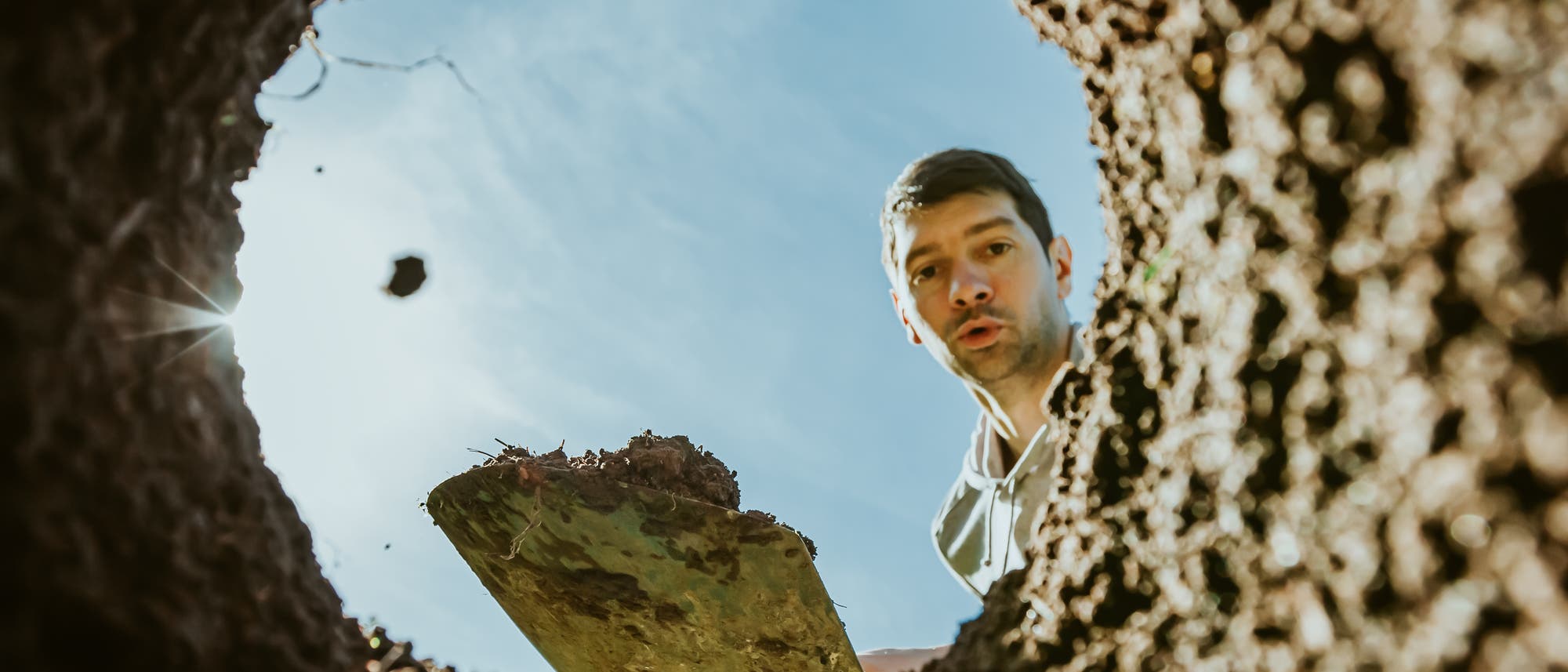 Eine Person blickt von oben in ein tiefes Erdloch, während sie eine Schaufel hält. Der Himmel ist klar und sonnig. Die Perspektive ist aus dem Inneren des Lochs nach oben gerichtet. Eine Person blickt von oben in ein tiefes Erdloch, während sie eine Schaufel hält. Der Himmel ist klar und sonnig. Die Perspektive ist aus dem Inneren des Lochs nach oben gerichtet.