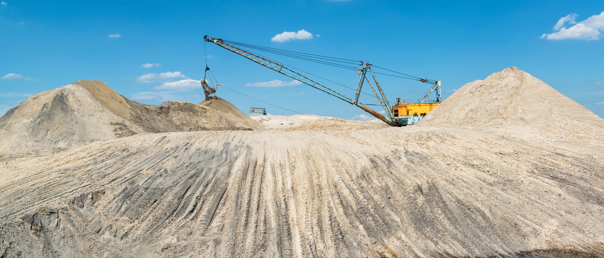 Eine große industrielle Baggermaschine fördert Sand auf einem Hügel in einem Tagebau. Eine große industrielle Baggermaschine fördert Sand auf einem Hügel in einem Tagebau.