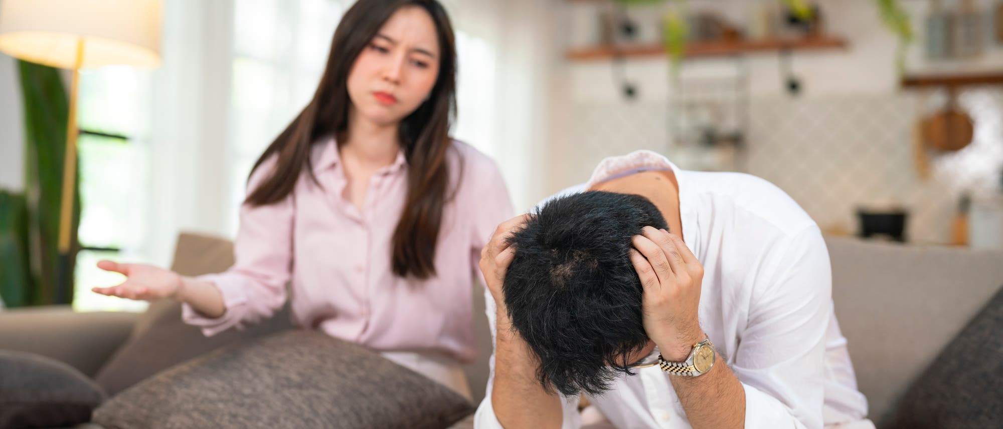 Eine Frau und ein Mann sitzen auf einem Sofa in einem Wohnzimmer. Die Frau gestikuliert mit einer Hand, während der Mann den Kopf in seine Hände stützt. Die Szene deutet auf eine angespannte oder emotionale Unterhaltung hin. Im Hintergrund sind eine Lampe, Pflanzen und Regale zu sehen. Eine Frau und ein Mann sitzen auf einem Sofa in einem Wohnzimmer. Die Frau gestikuliert mit einer Hand, während der Mann den Kopf in seine Hände stützt. Die Szene deutet auf eine angespannte oder emotionale Unterhaltung hin. Im Hintergrund sind eine Lampe, Pflanzen und Regale zu sehen.