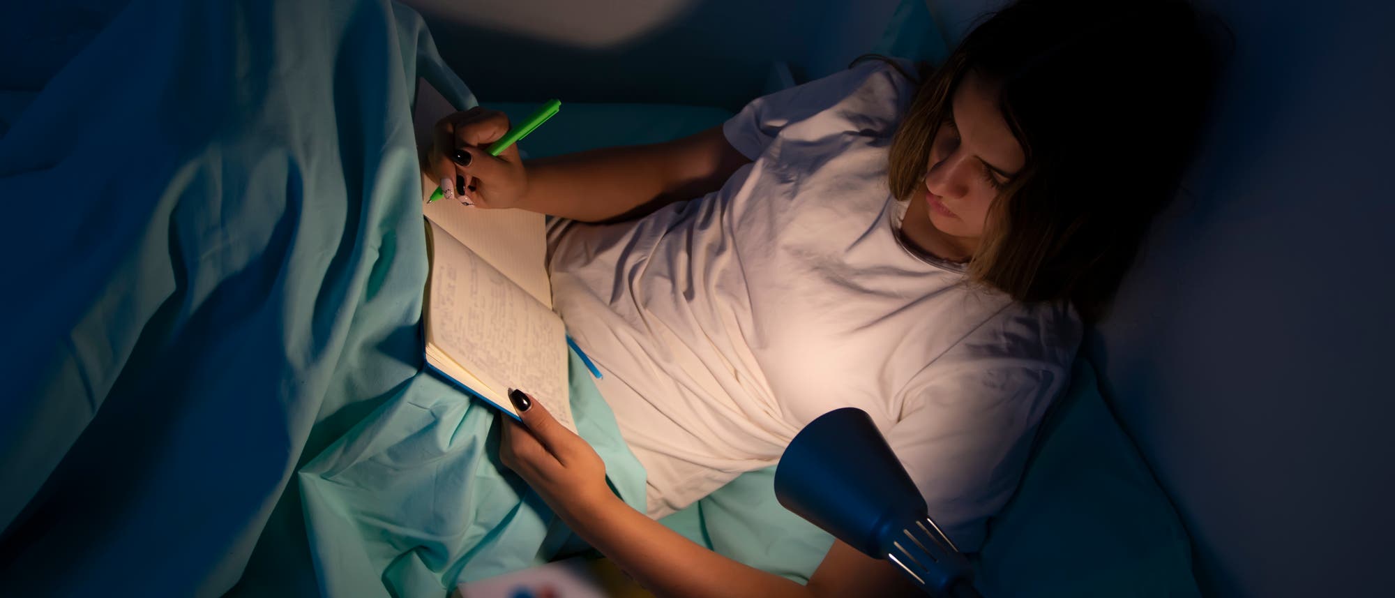 Eine junge Frau sitzt im Bett und schreibt in ein Notizbuch.