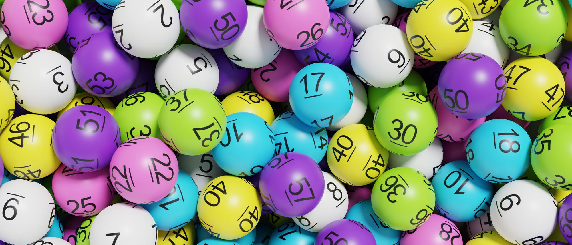 Ein Haufen bunter Lottokugeln mit aufgedruckten Zahlen. Die Kugeln sind in verschiedenen Farben wie Blau, Gr&uuml;n, Gelb, Lila und Wei&szlig; gehalten. Jede Kugel tr&auml;gt eine schwarze Zahl, die von 1 bis 57 reicht. Die Kugeln sind zuf&auml;llig angeordnet und &uuml;berlappen sich teilweise.